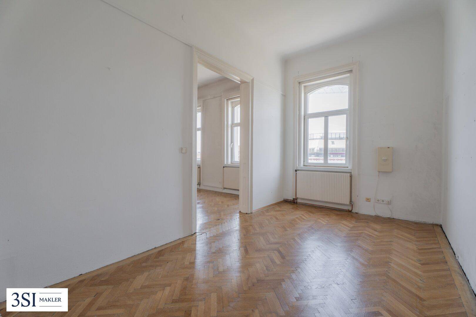 Geräumiges Zimmer mit klassischem Fischgrätparkett und einem großen Fenster.