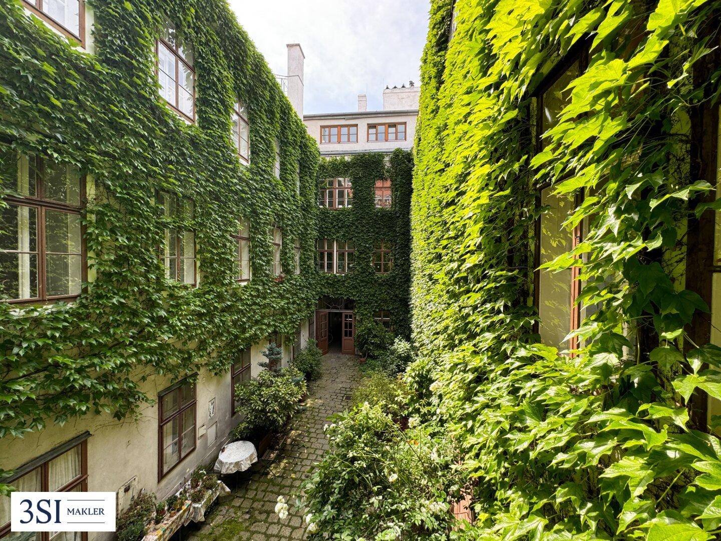 Blick in einen begrünten Innenhof, dessen Wände vollständig mit Efeu bewachsen sind und eine ruhige Atmosphäre bieten.