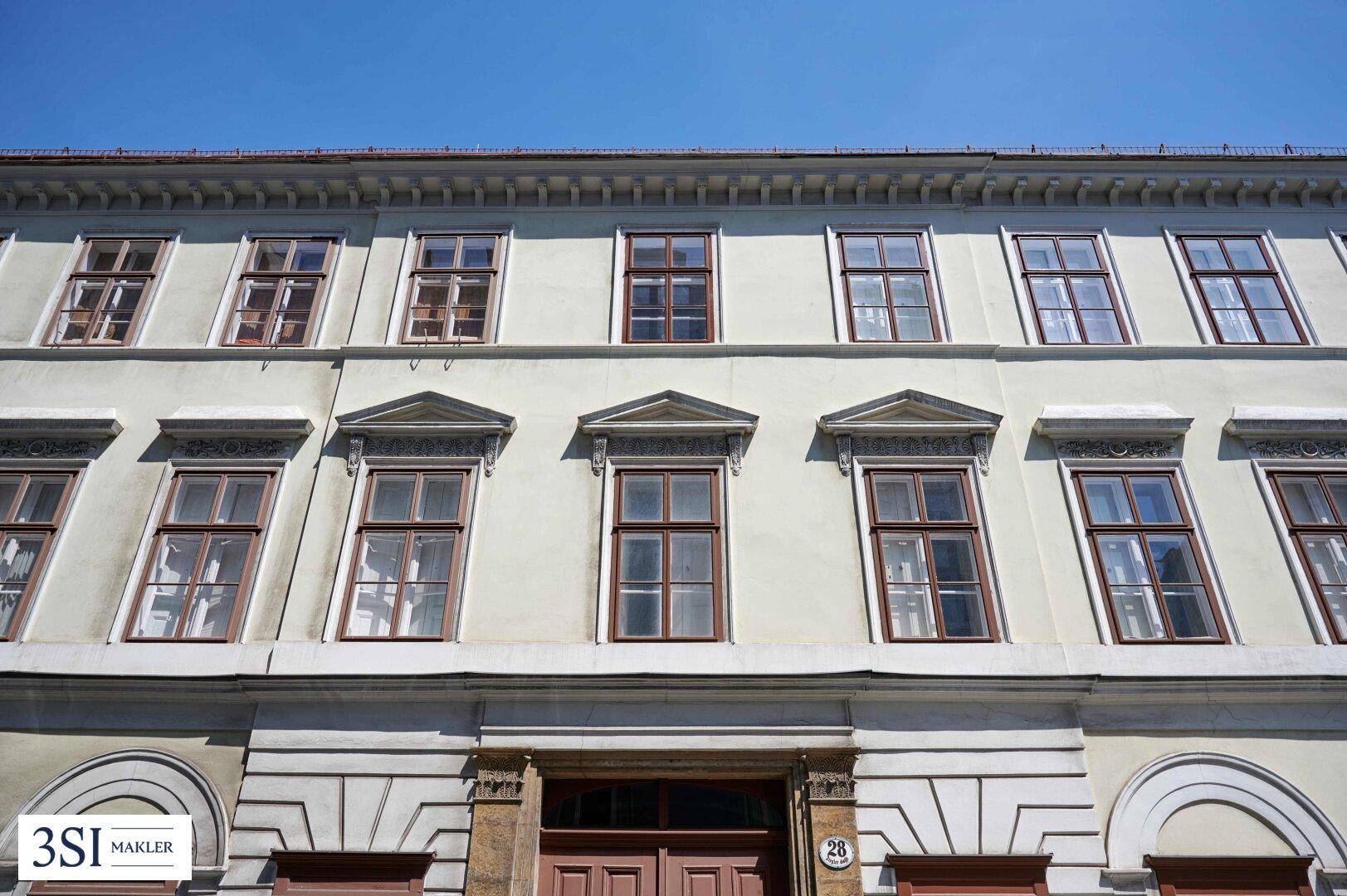 Detailansicht einer historischen Fassade mit vielen Fenstern und dekorativen Elementen über dem Eingangsbereich.