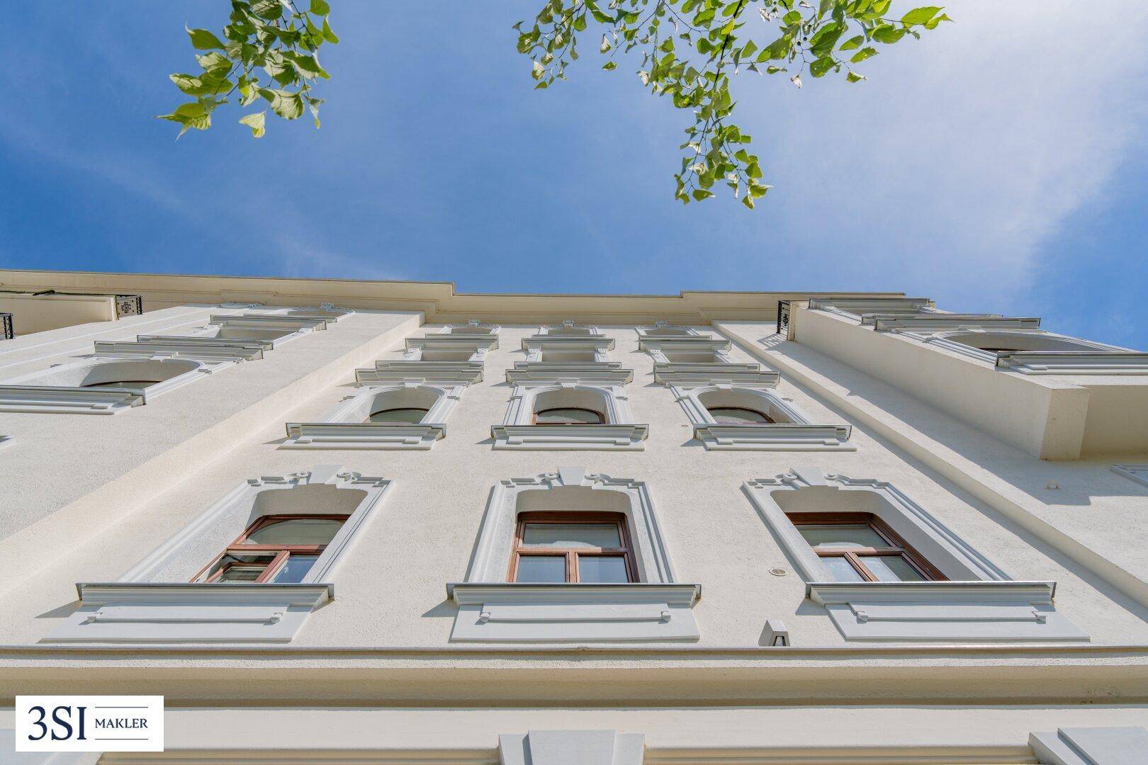 Fassadenansicht eines Gebäudes mit vielen Fenstern und dekorativen Elementen unter blauem Himmel.