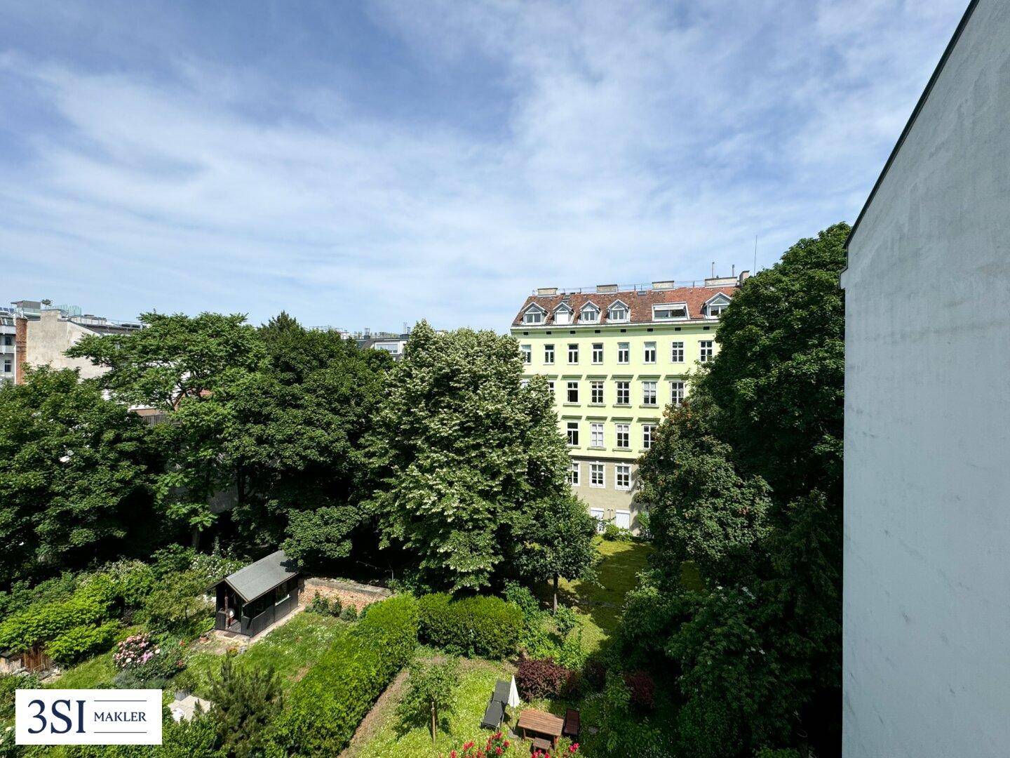 Panoramablick auf einen ruhigen Stadtgarten mit üppiger Vegetation und angrenzenden Wohngebäuden.