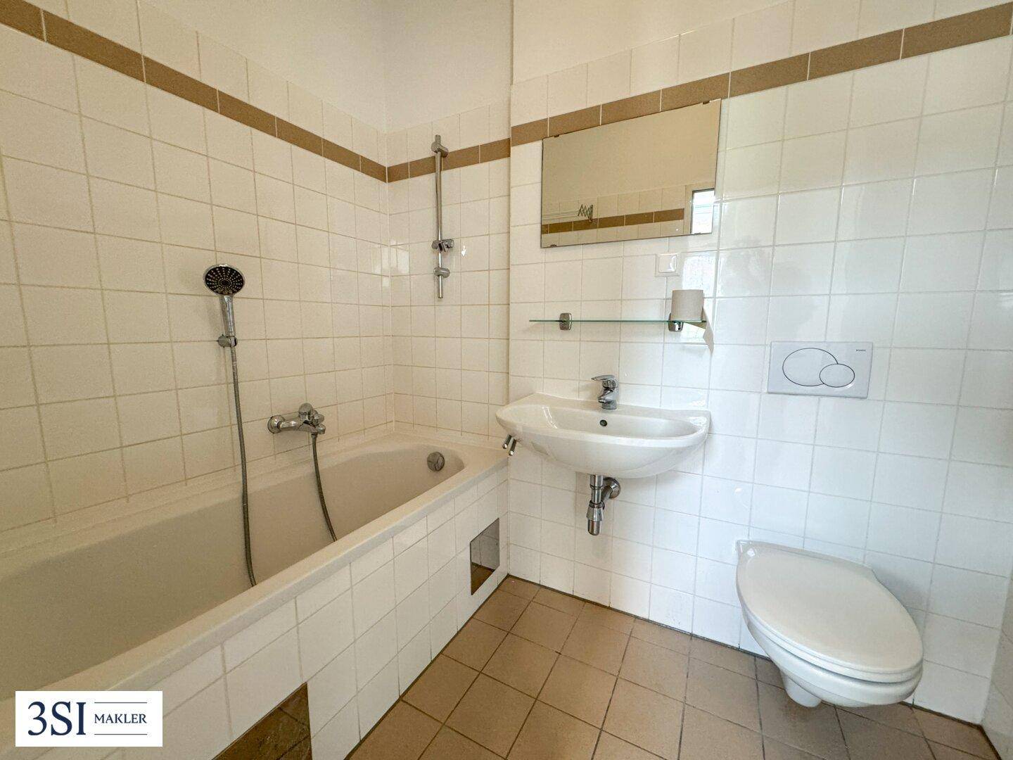 Gefliestes Badezimmer mit Badewanne, Duschfunktion, Waschbecken und wandhängendem WC in hellem Design.