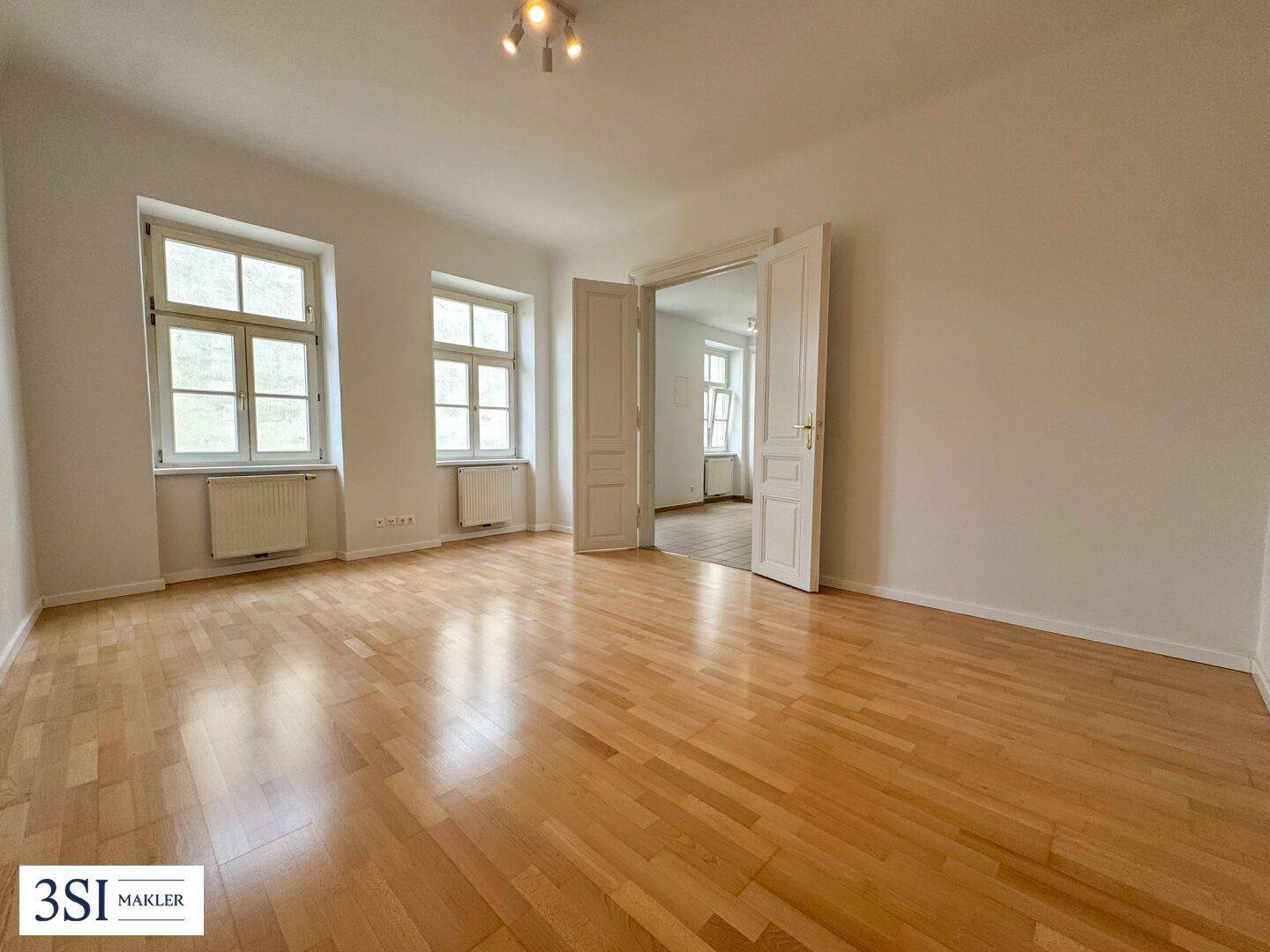 Geräumiges, helles Zimmer mit glänzendem Parkettboden und zwei großen Fenstern, die viel Licht hereinlassen.