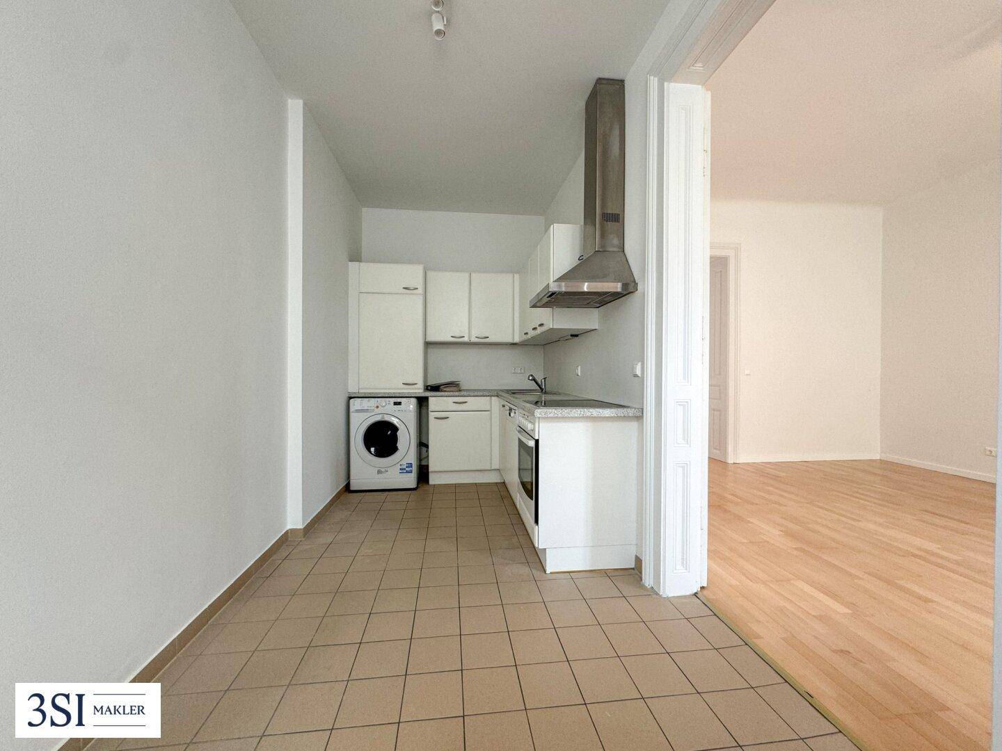 Kleine Einbauküche mit weißen Schränken, Herd, Backofen und Waschmaschine, offen zum Wohnbereich.