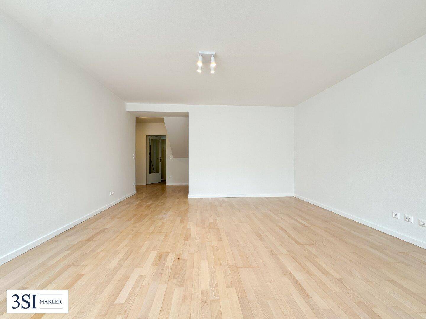Heller Wohnbereich mit Holzboden und Zugang zu einem Flur mit Treppe, bereit zur individuellen Gestaltung.