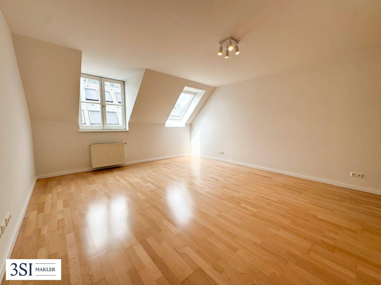 Geräumiger Dachbodenraum mit hellem Holzboden und viel Tageslicht durch Dachfenster und Gaubenfenster.