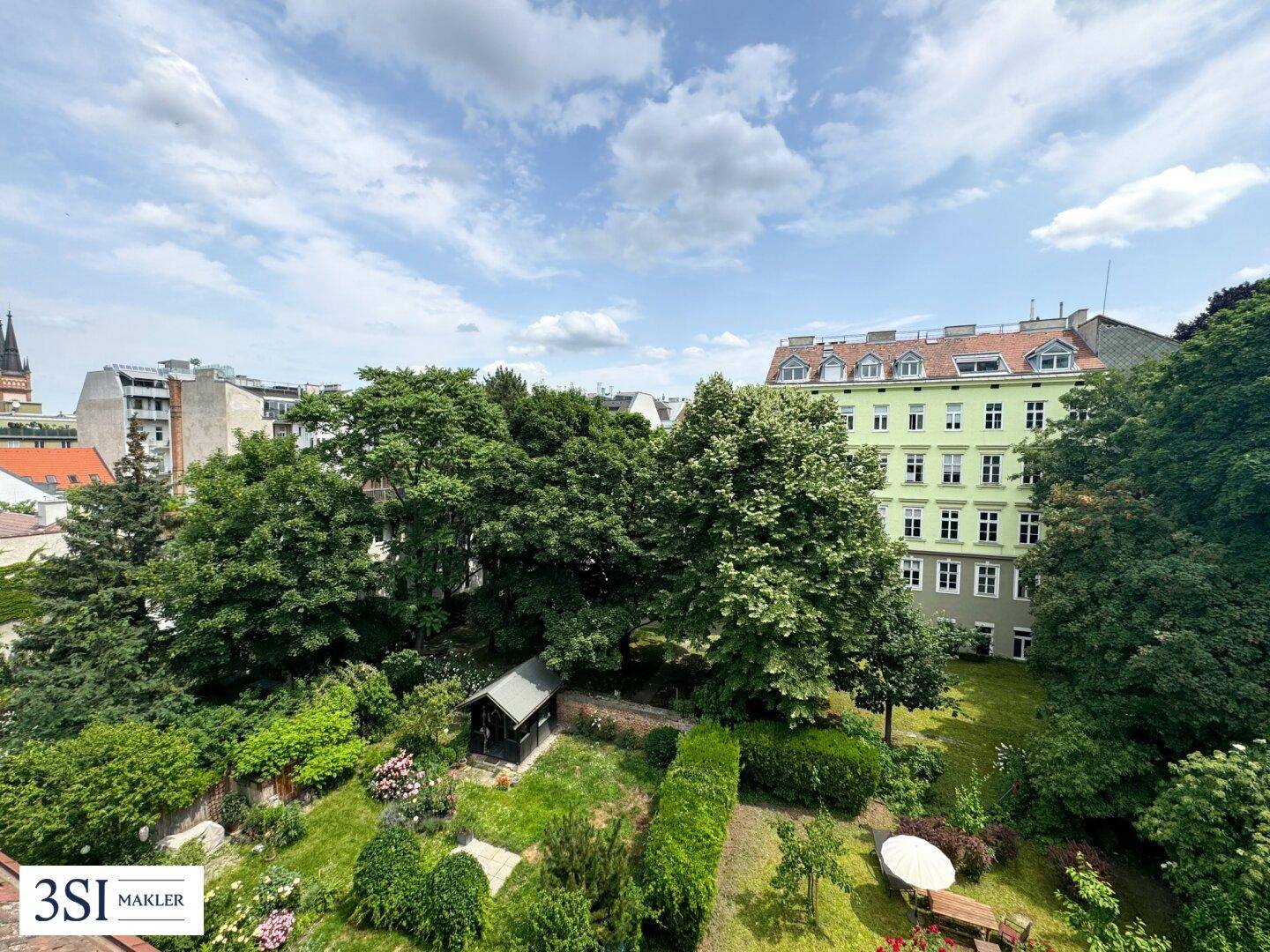 Weitläufiger grüner Gartenbereich mit altem Baumbestand und einem Gartenhaus, umgeben von Stadtgebäuden.