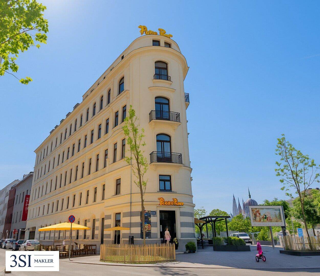 Modernes Eckgebäude mit Restaurant im Erdgeschoss und belebter Stadtansicht unter strahlendem Sonnenschein.