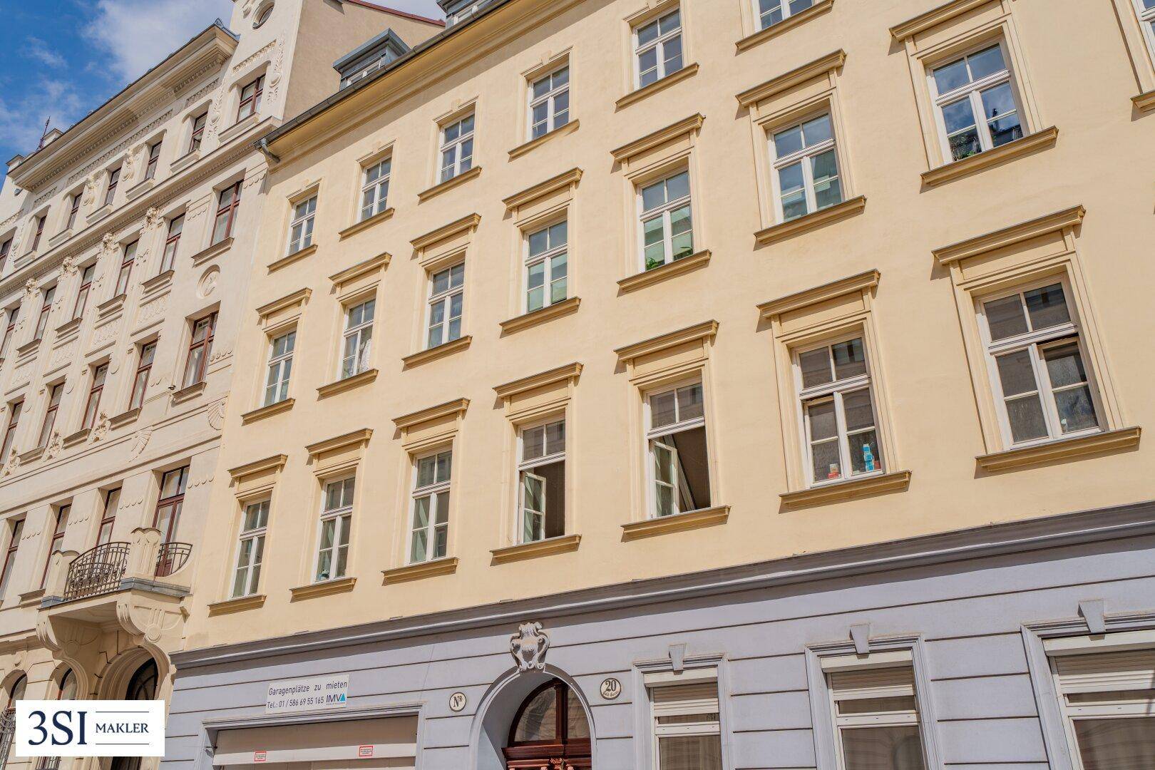 Detailansicht der beigen Fassade eines Altbaus mit zahlreichen Fenstern und dekorativen Elementen.