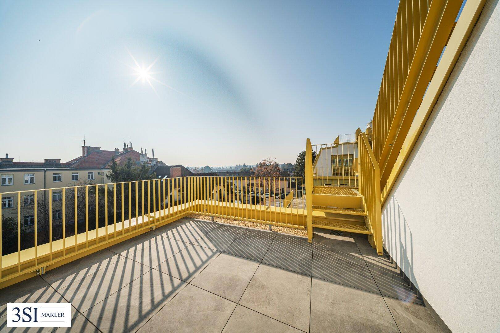 Sonnige Dachterrasse mit leuchtend gelbem Geländer und weitem Blick über die Stadt.