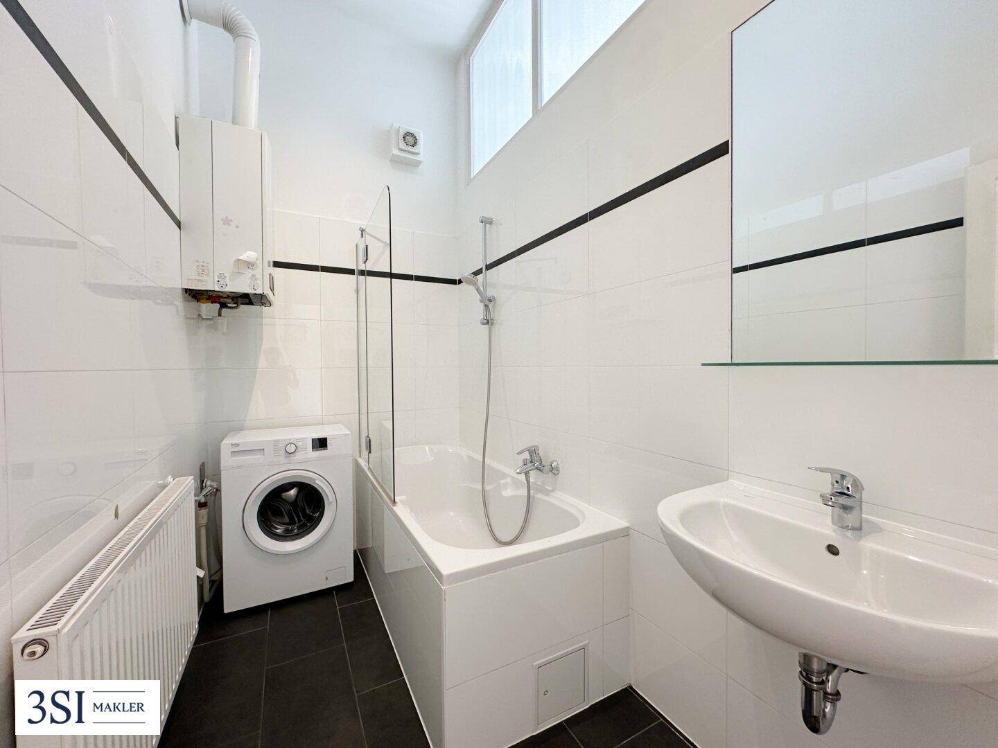 Funktionales Badezimmer mit Badewanne, Waschmaschine und Gastherme an der Wand.