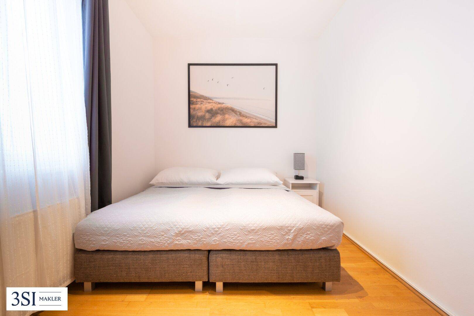 Helles Schlafzimmer mit Holzboden, einem Doppelbett und schlichter Wanddekoration.