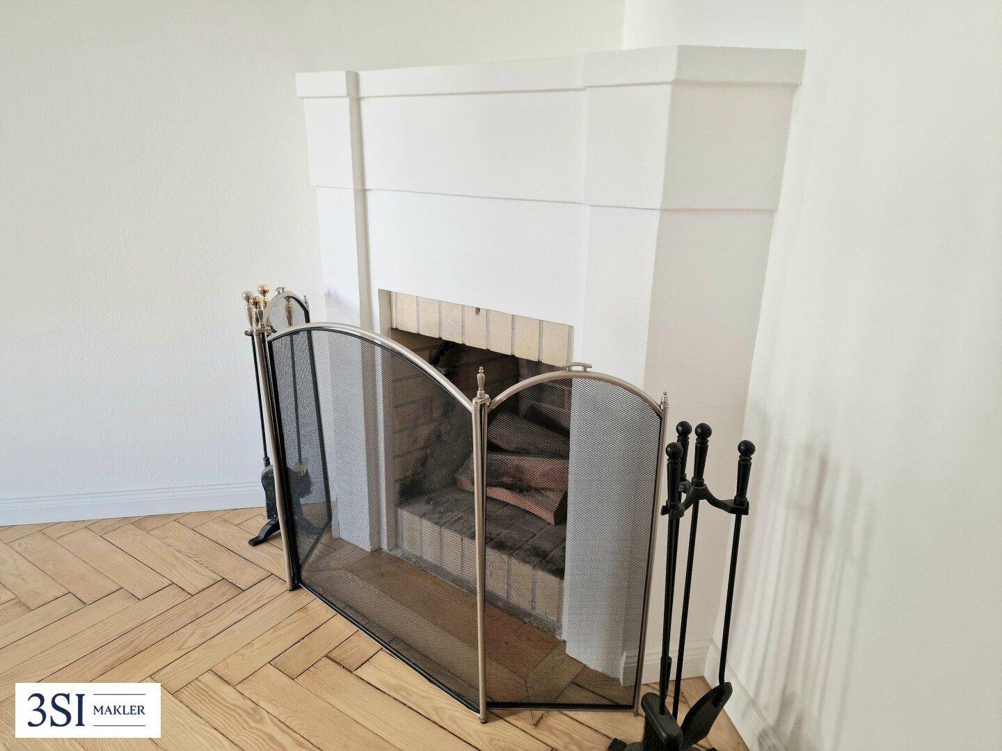 Klassischer Kamin mit Kaminschutzgitter in einem hellen Raum mit Fischgrätparkett.