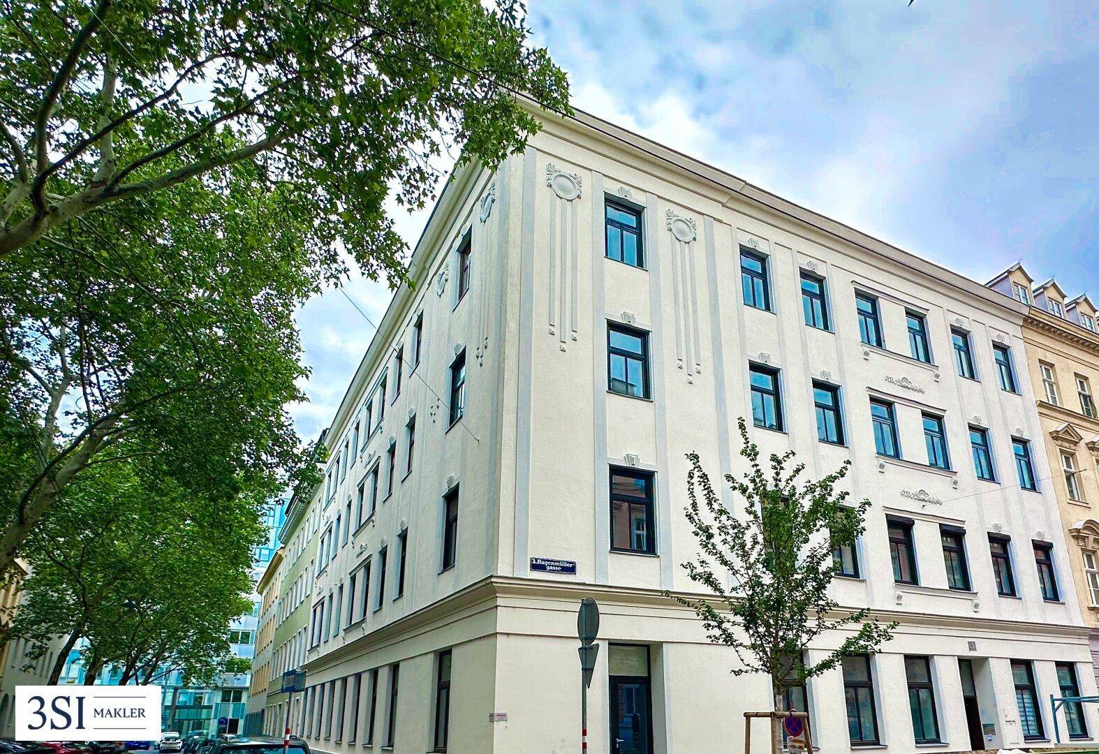 Historisches Eckgebäude mit klassischer Fassade und vielen Fenstern, umgeben von Bäumen.