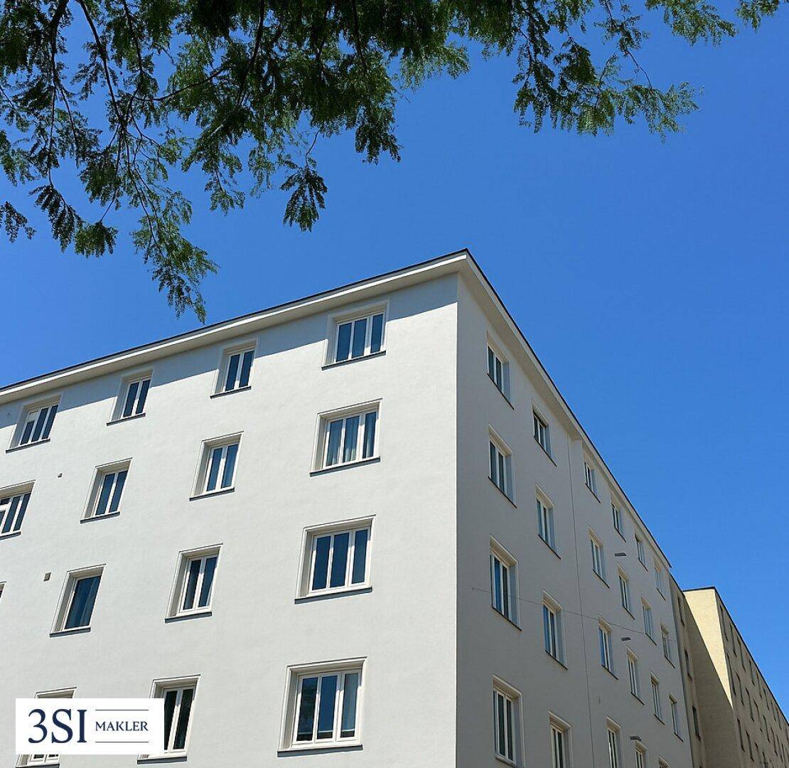 Moderne weiße Gebäudefassade mit vielen Fenstern unter einem klaren blauen Himmel.