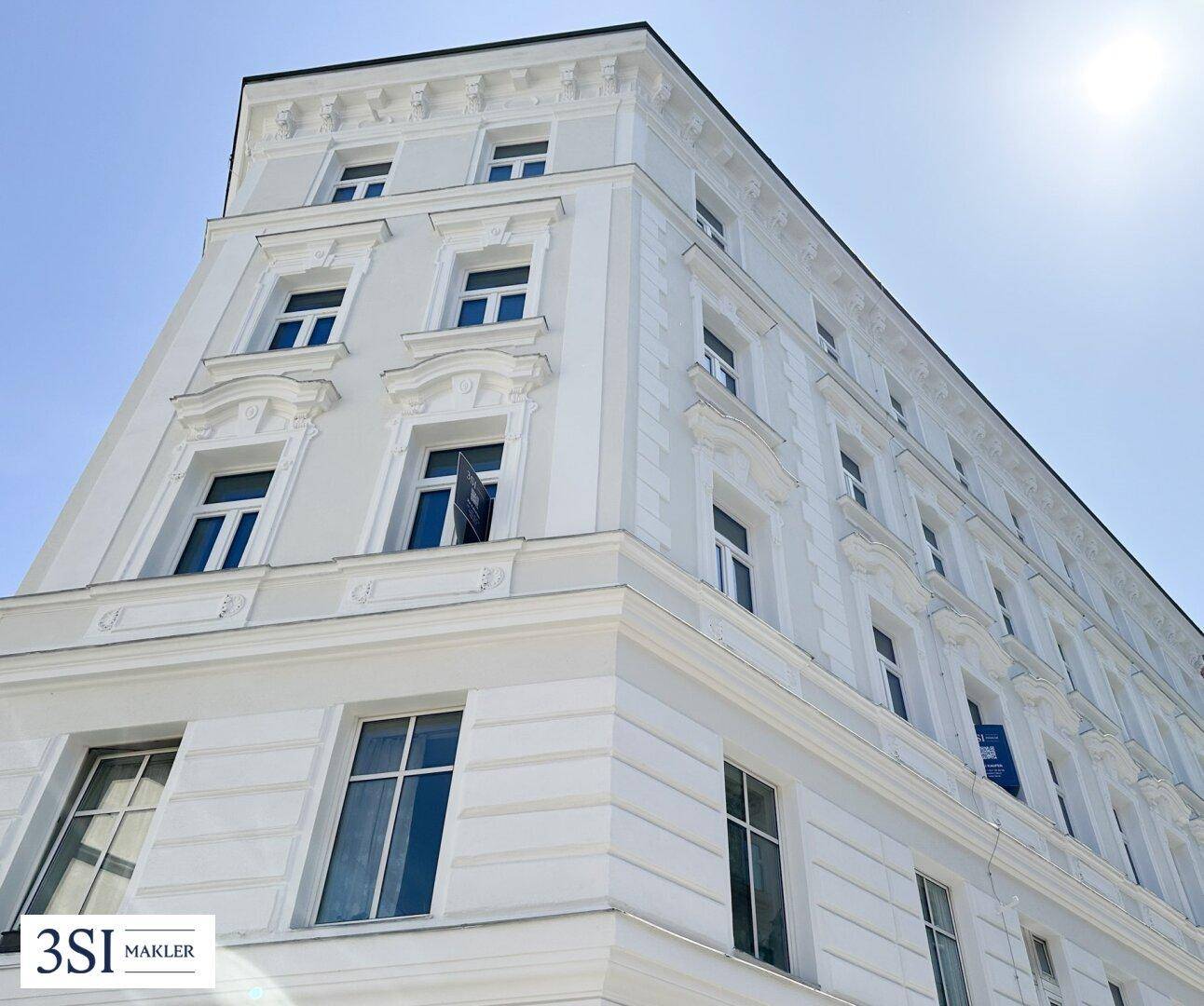 Detailansicht der frisch renovierten Fassade eines Altbaus mit Stuckelementen unter blauem Himmel.