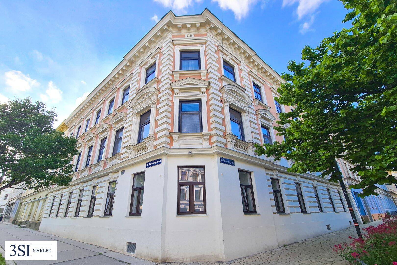 Prächtiges Eckgebäude mit historischer, reich verzierter Fassade in Rosa und Weiß unter blauem Himmel.
