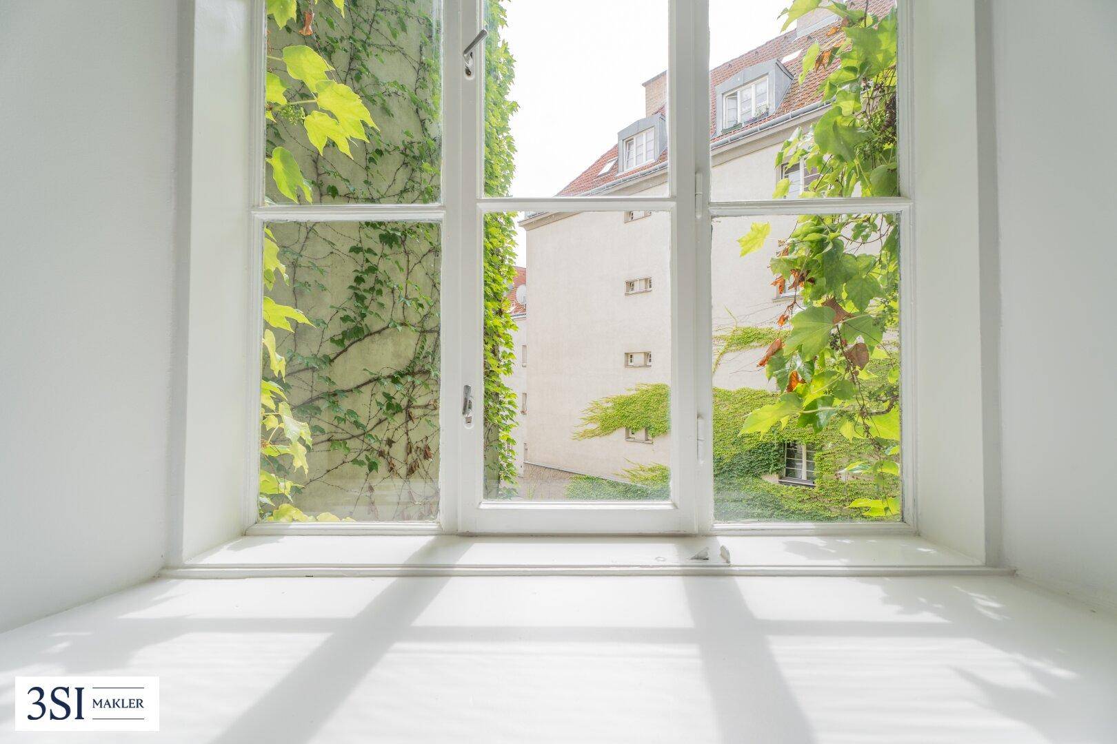 Fensterblick auf einen begrünten Innenhof mit viel Tageslicht.
