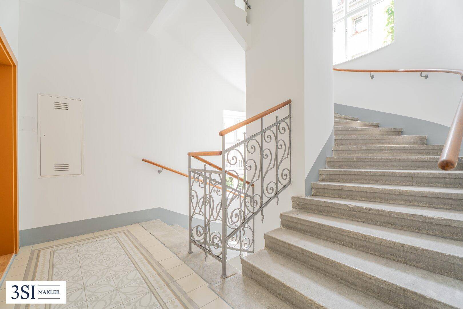Historisches Treppenhaus mit Steinstufen und gemusterten Fliesen im Eingangsbereich.