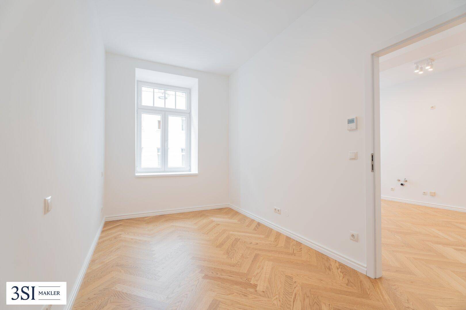 Helles, leeres Zimmer mit Fischgrätparkett und einem Fenster, ideal als Schlaf- oder Arbeitszimmer.