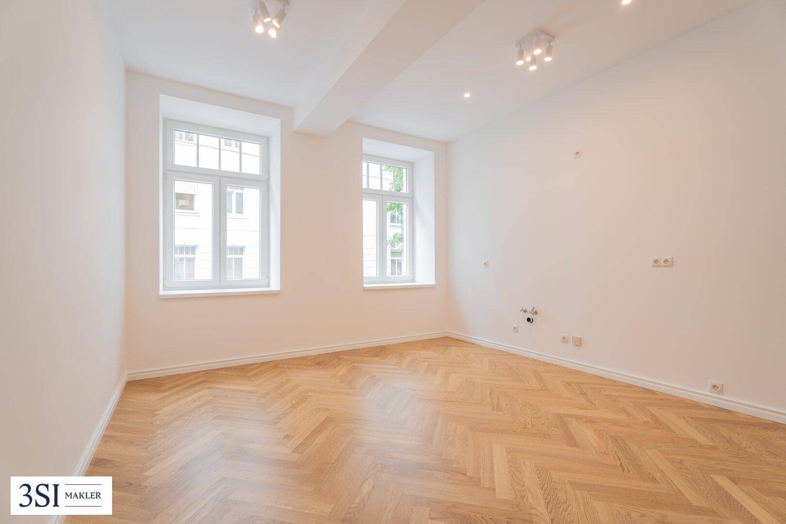 Großes, unmöbliertes Zimmer mit Fischgrätparkett und zwei Fenstern, bietet viel Gestaltungspotenzial.