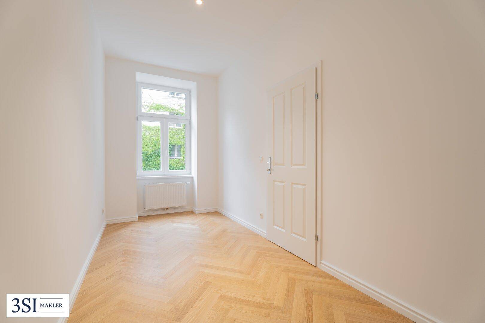 Kleineres Zimmer mit Fischgrätparkett und einem Fenster zum begrünten Innenhof.