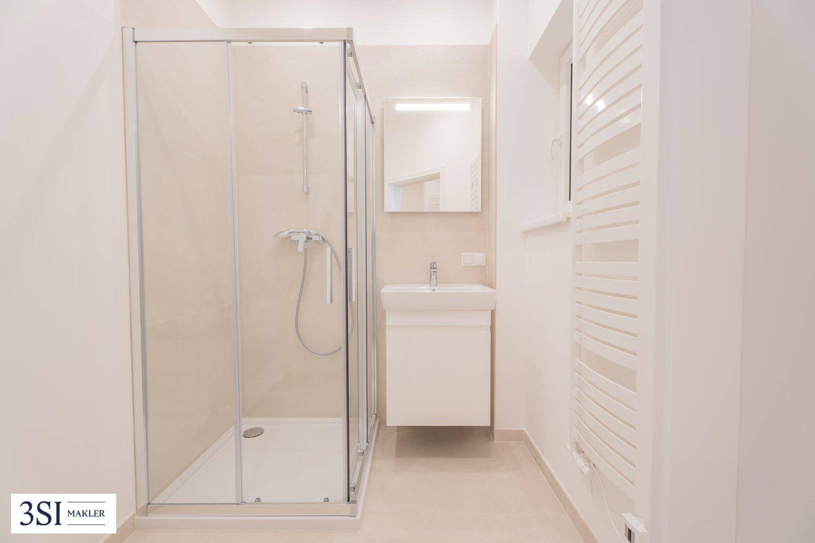 Modernes Badezimmer mit Duschkabine, Waschtisch und beheiztem Handtuchhalter in hellen Farbtönen.