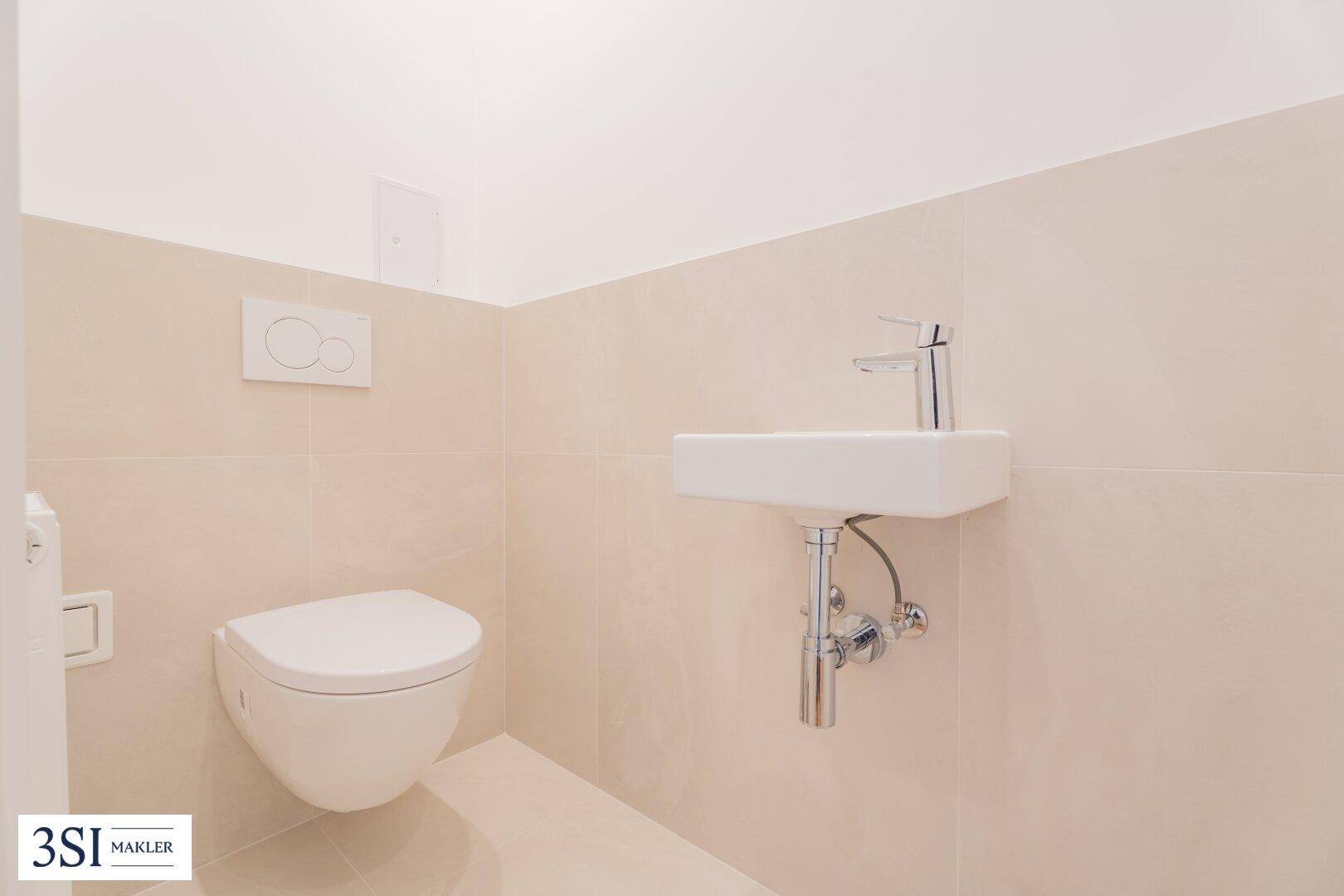 Separates WC mit wandhängender Toilette und kleinem Handwaschbecken, in neutralen Farben gehalten.