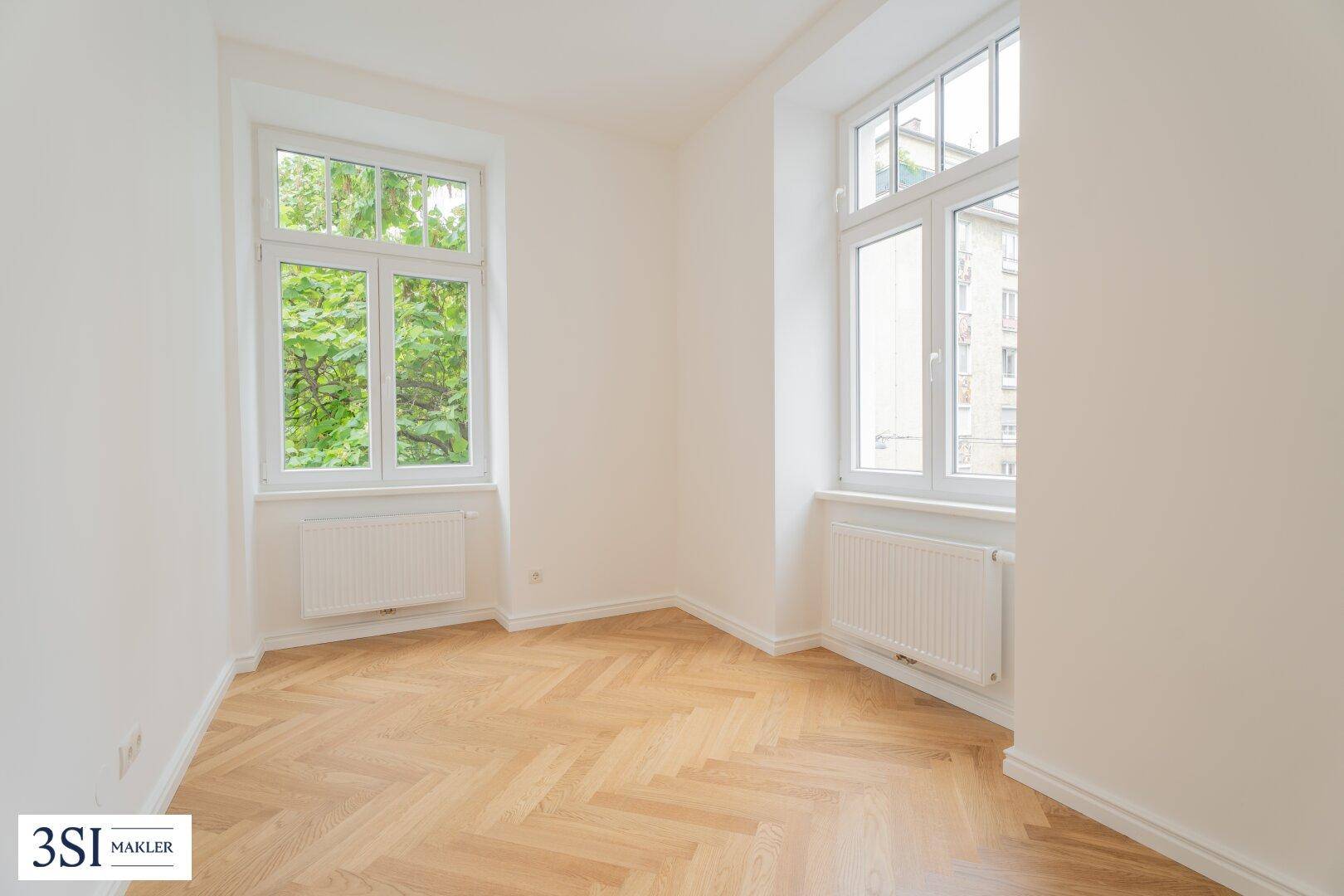 Gemütliches Zimmer mit Fischgrätparkett und grünem Ausblick, ideal als Schlaf- oder Arbeitszimmer.