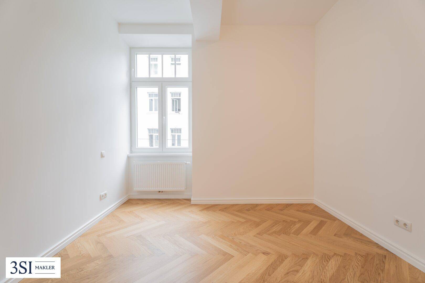 Ruhiges Zimmer mit Fischgrätparkett und einem Fenster, bietet eine angenehme Atmosphäre.