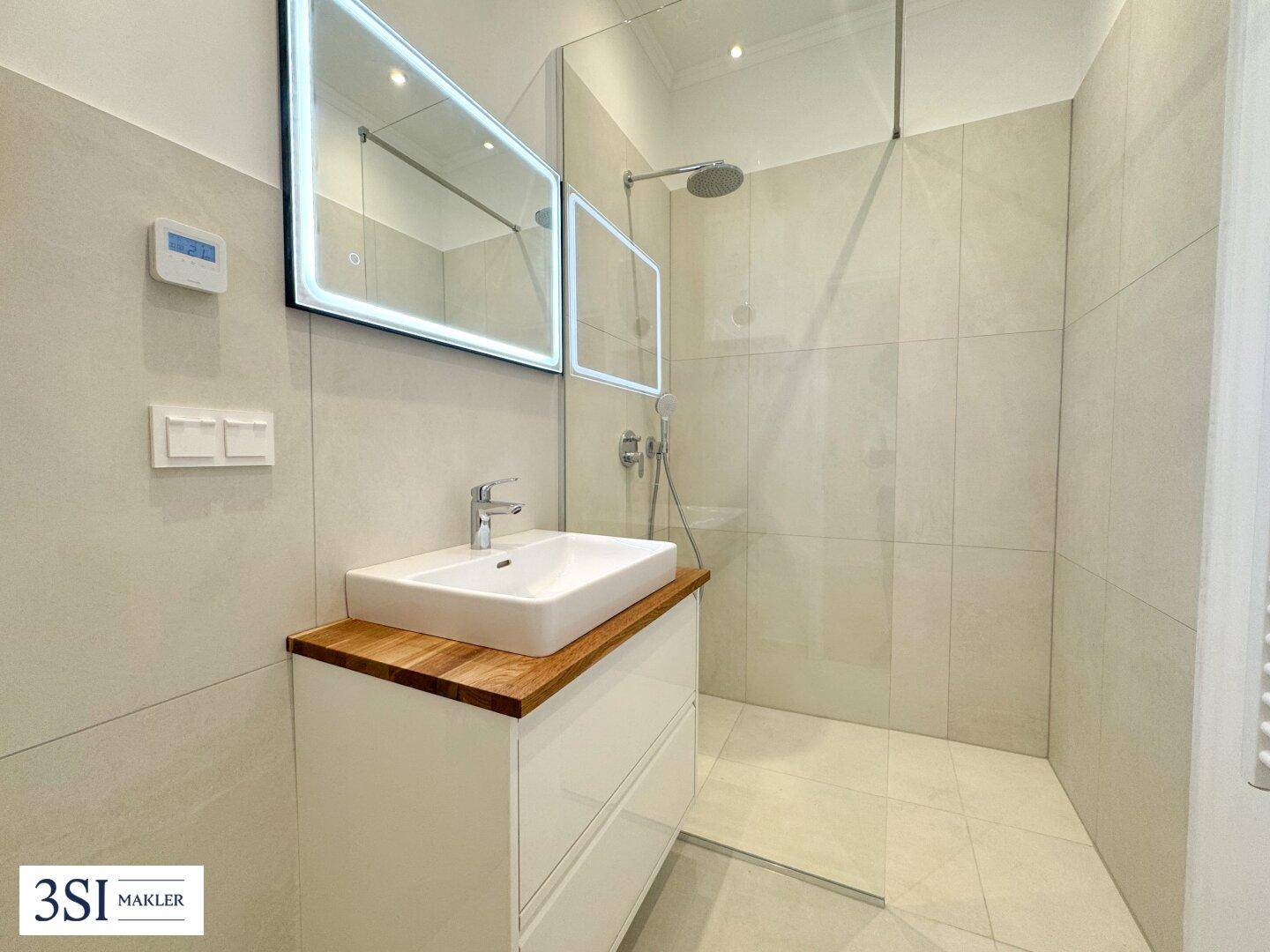 Modernes Badezimmer mit begehbarer Dusche, Einzelwaschbecken und beleuchtetem Spiegel.