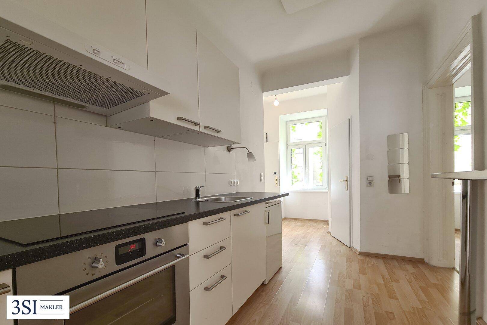 Funktionale Küche mit weißen Schränken, dunkler Arbeitsplatte und Blick in einen weiteren Raum.