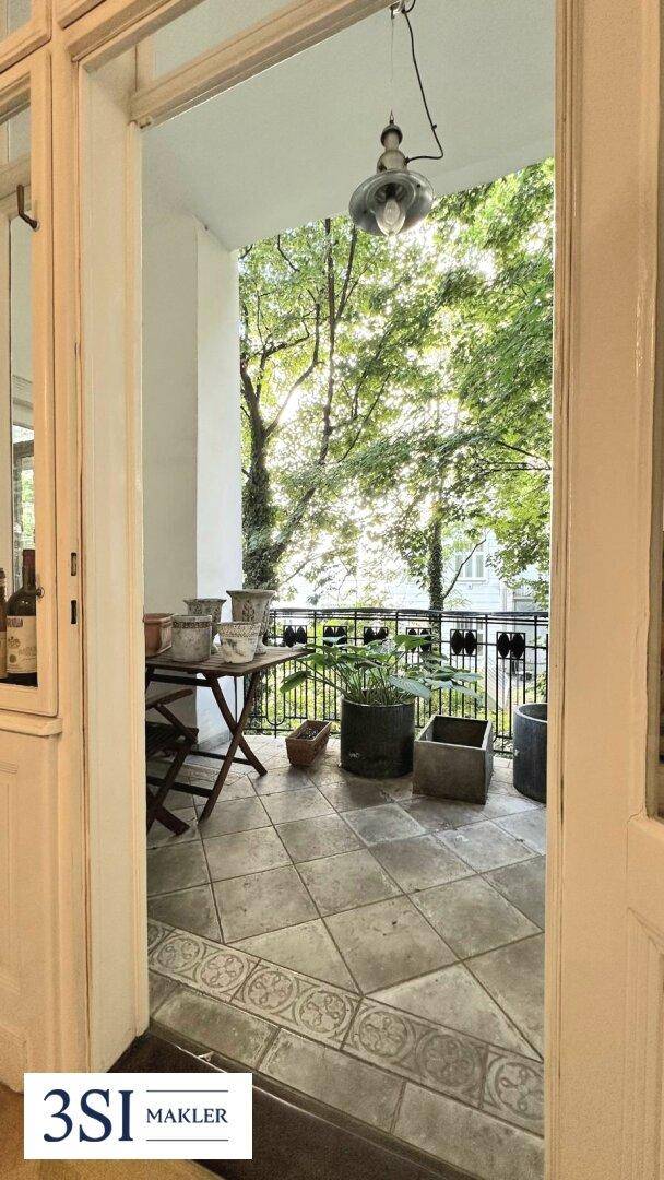 Grüner Balkon mit Fliesenboden und Topfpflanzen, umgeben von Bäumen.