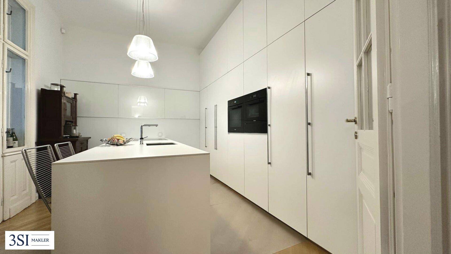 Moderne weiße Küche mit Kücheninsel, integrierten Geräten und minimalistischem Design.
