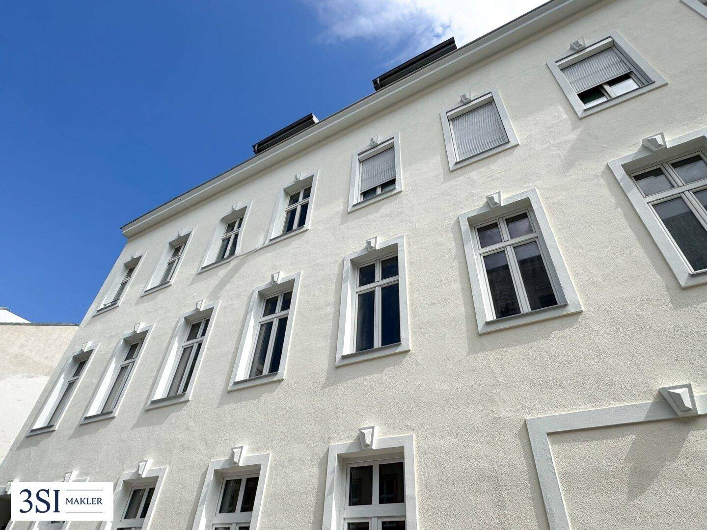 Klassische Fassade eines Mehrfamilienhauses mit vielen Fenstern unter blauem Himmel.