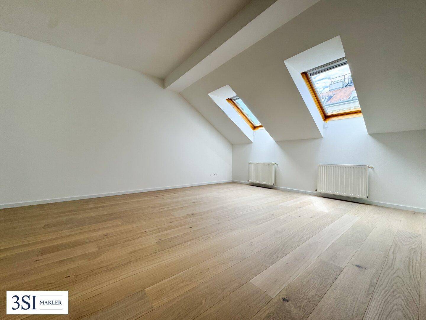 Lichtdurchflutetes Dachgeschosszimmer mit Holzboden und zwei Dachfenstern, ideal für ein Schlafzimmer.