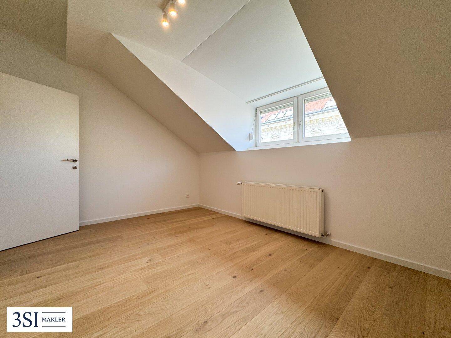 Gemütliches Zimmer im Dachgeschoss mit Holzboden und schrägen Wänden, ideal als Schlaf- oder Arbeitszimmer.