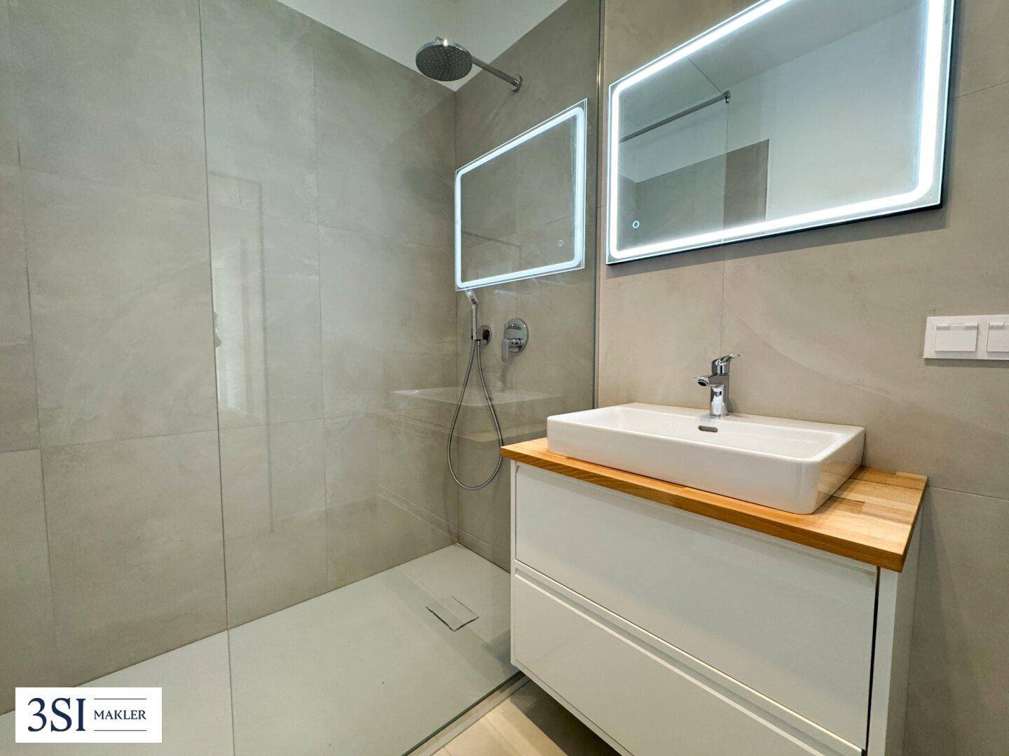 Modernes Badezimmer mit begehbarer Dusche, großformatigen Fliesen und beleuchteten Spiegeln.