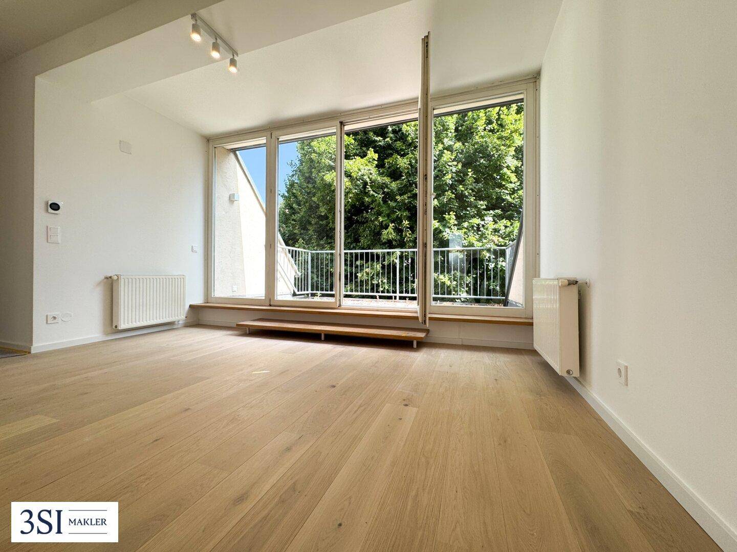 Geräumiges Wohnzimmer mit Holzboden und großen Fenstern, die Zugang zu einem französischen Balkon bieten.