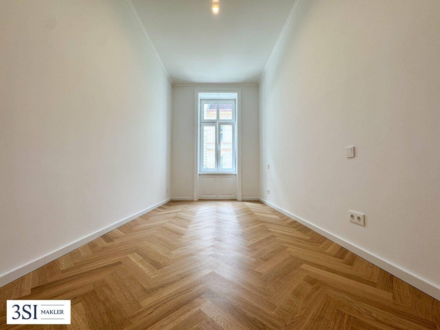 Heller, leerer Raum mit einem Fenster und elegantem Fischgrätparkettboden, frisch renoviert.