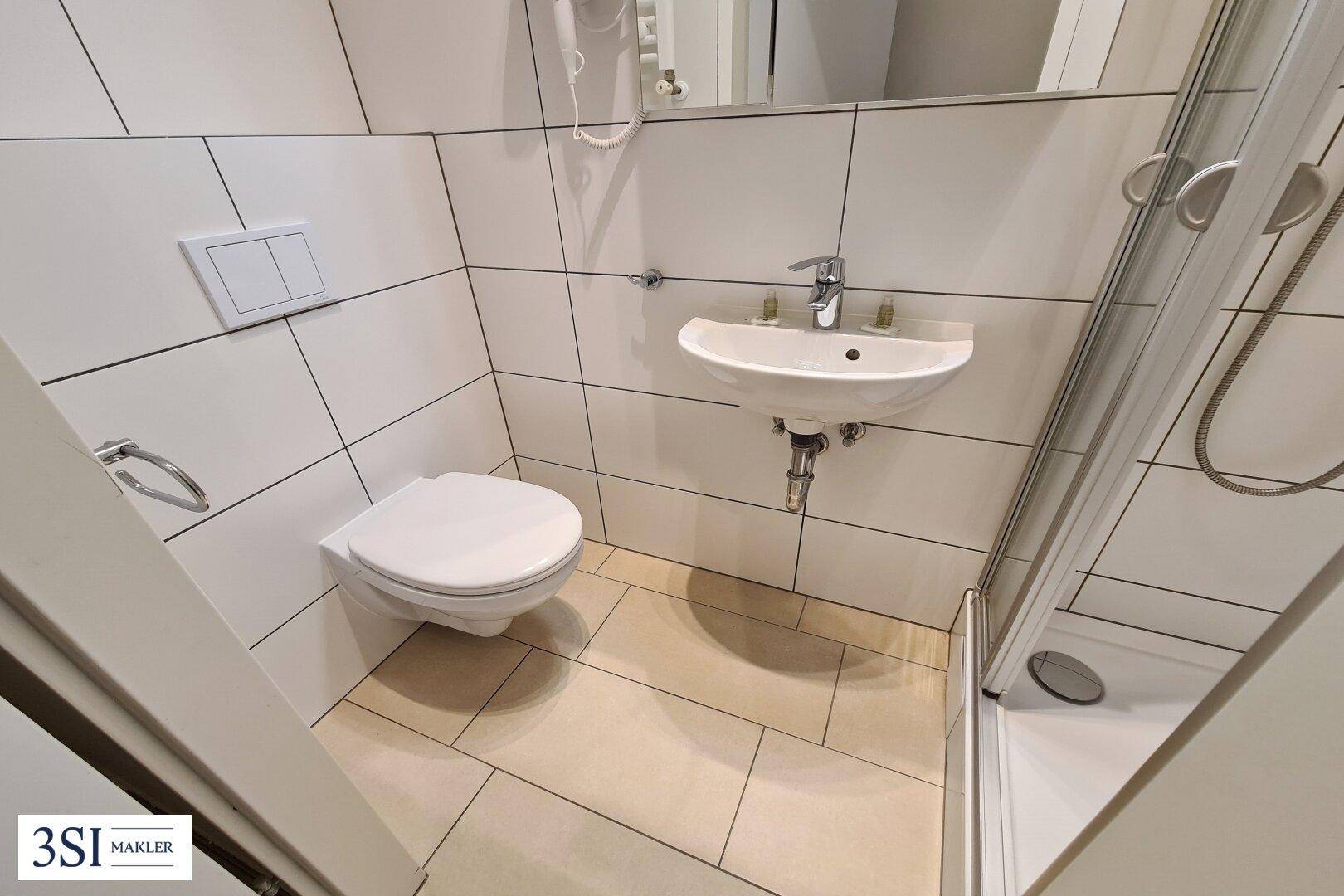 Modern gefliestes Badezimmer mit Dusche, WC und Waschbecken in hellen Farbtönen.