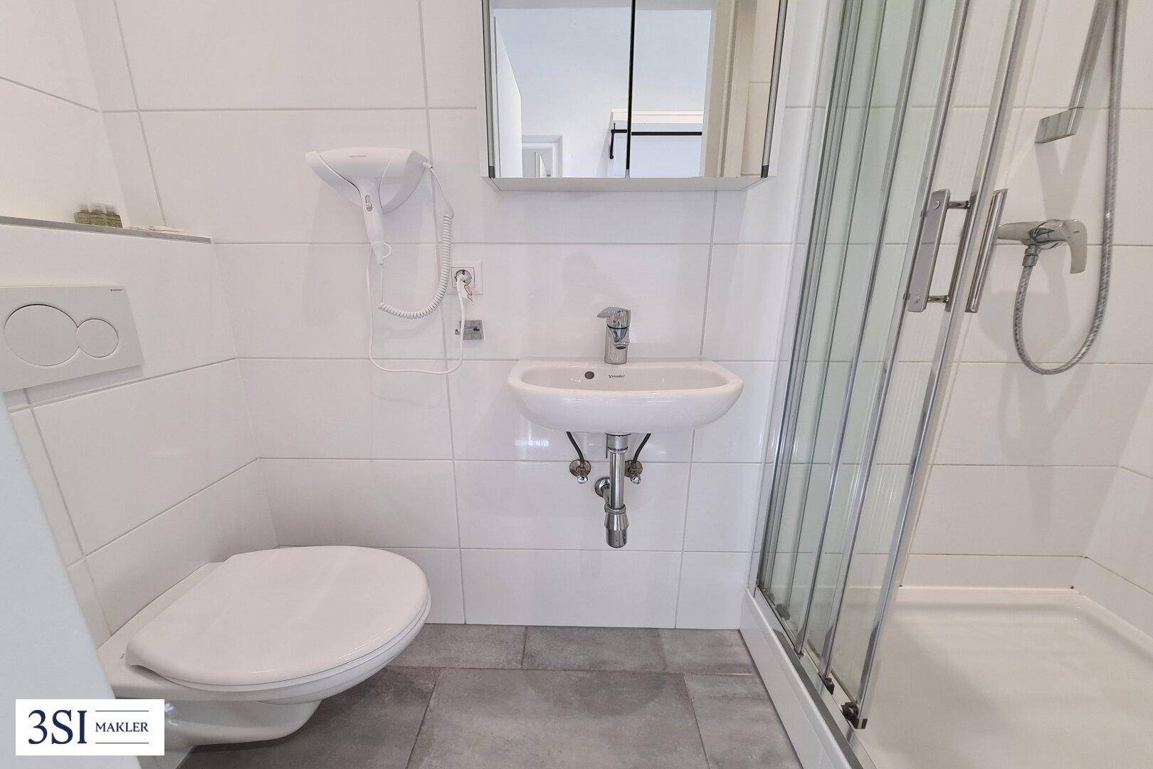 Kleines Badezimmer mit weiß gefliesten Wänden, Toilette und Duschkabine.