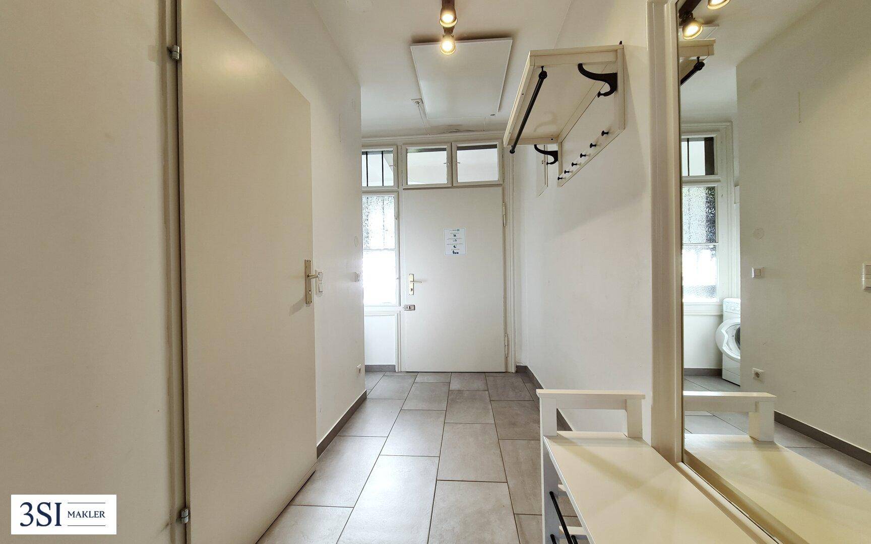 Heller Eingangsbereich mit Fliesenboden, Garderobe und großem Spiegel.