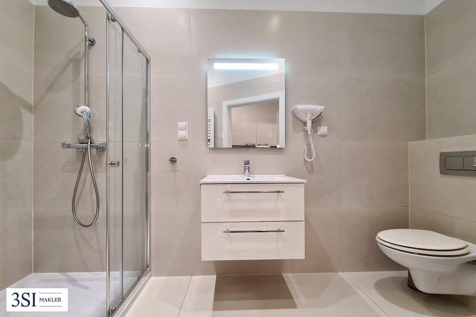Modernes Badezimmer mit Duschkabine, wandhängendem WC und großformatigen Fliesen.