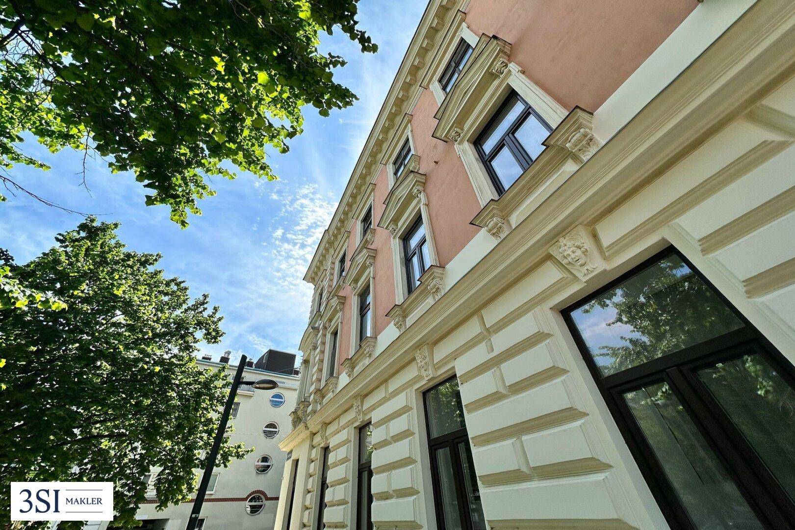 Historische Fassade eines Gebäudes mit dekorativen Elementen und grünen Bäumen.