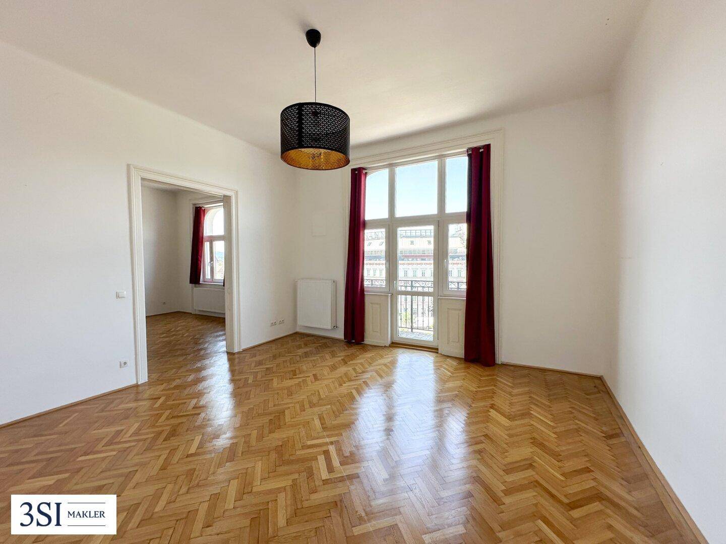 Geräumiger Wohnbereich mit klassischem Fischgrätparkett und Zugang zu einem französischen Balkon.