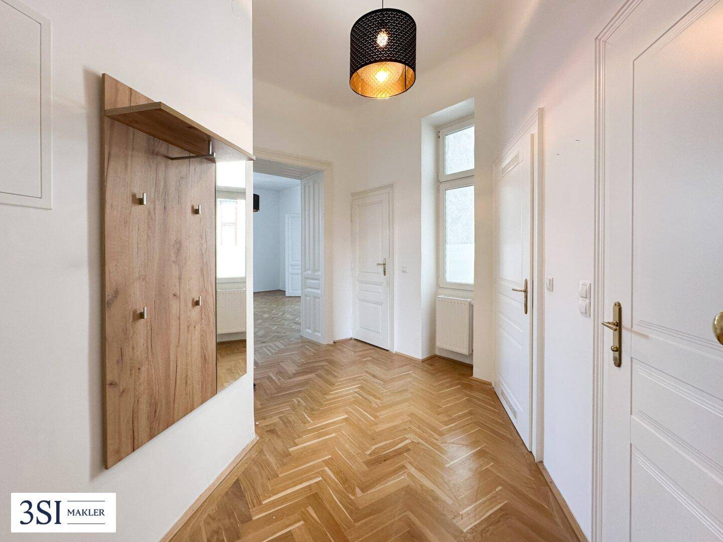 Heller Flur mit Fischgrätparkett, weiß gestrichenen Türen und einem modernen Garderobenspiegel.