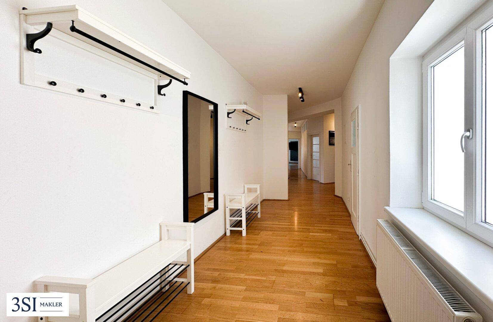 Heller Flur mit Garderobe, Spiegel und Holzboden, der zu weiteren Räumen führt.
