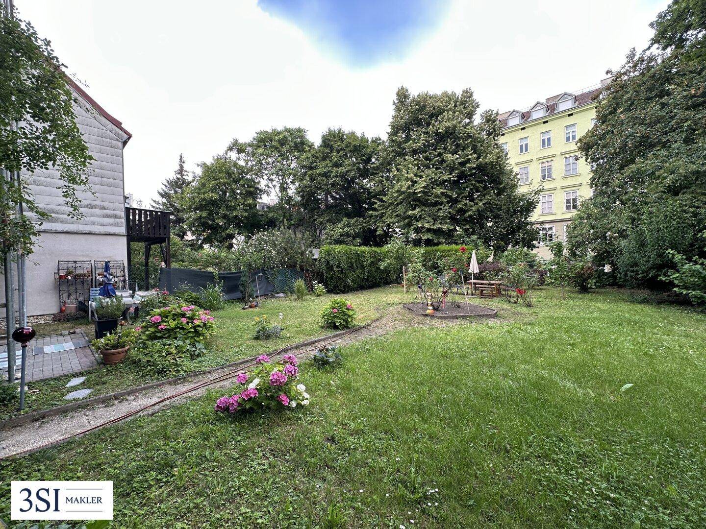Großer, gepflegter Garten mit Rasenfläche, Blumenbeeten und Sitzgelegenheiten im Freien.