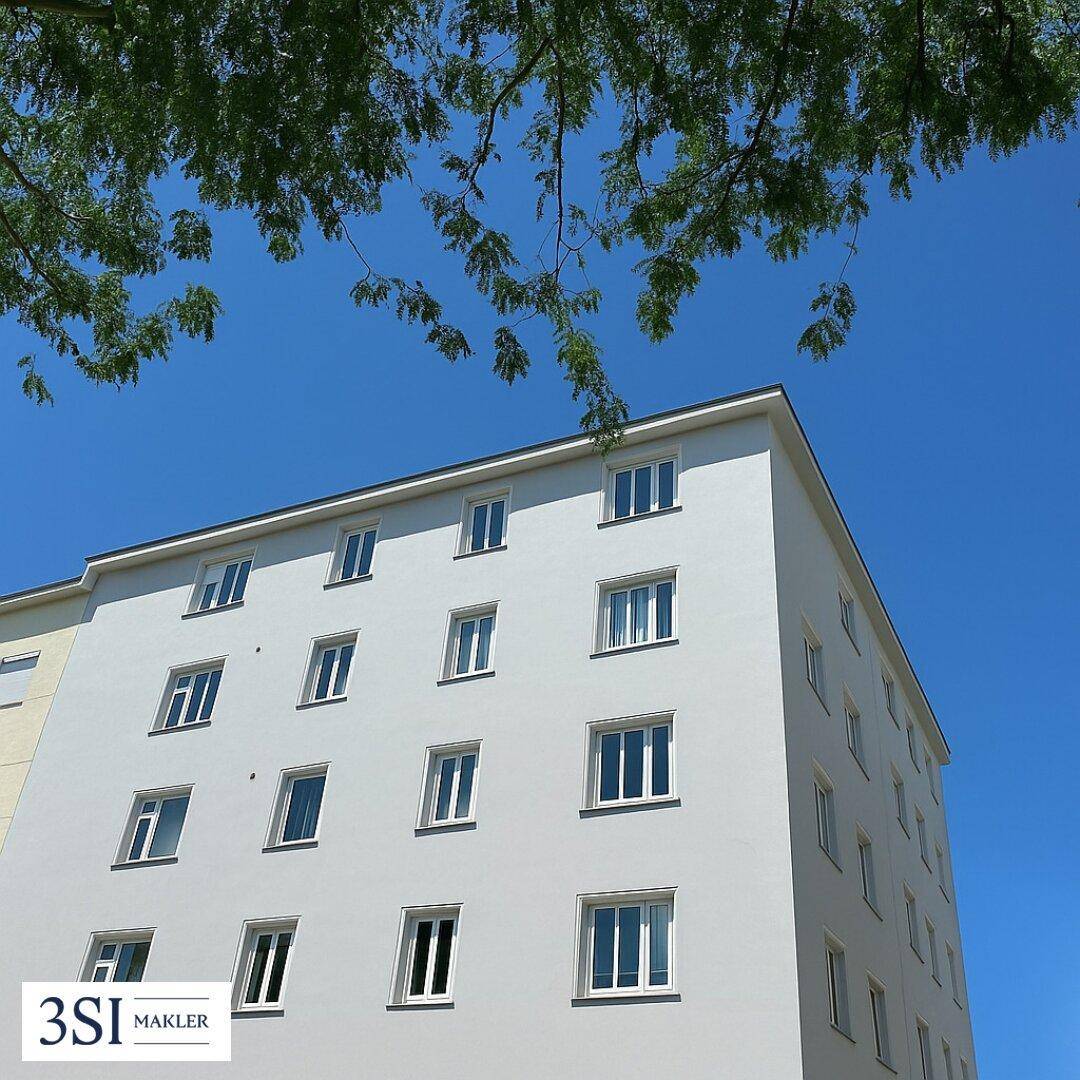 Moderne Gebäudefassade mit vielen Fenstern unter einem strahlend blauen Himmel und Bäumen.